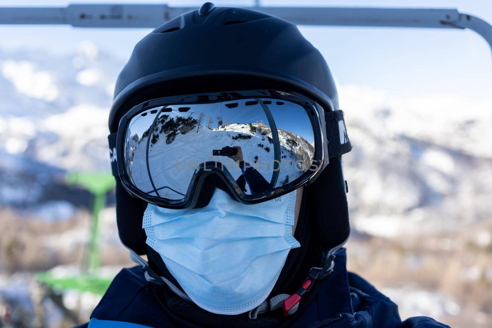 ski resort man on chairlift in helmet and medical mask by Chechotkin