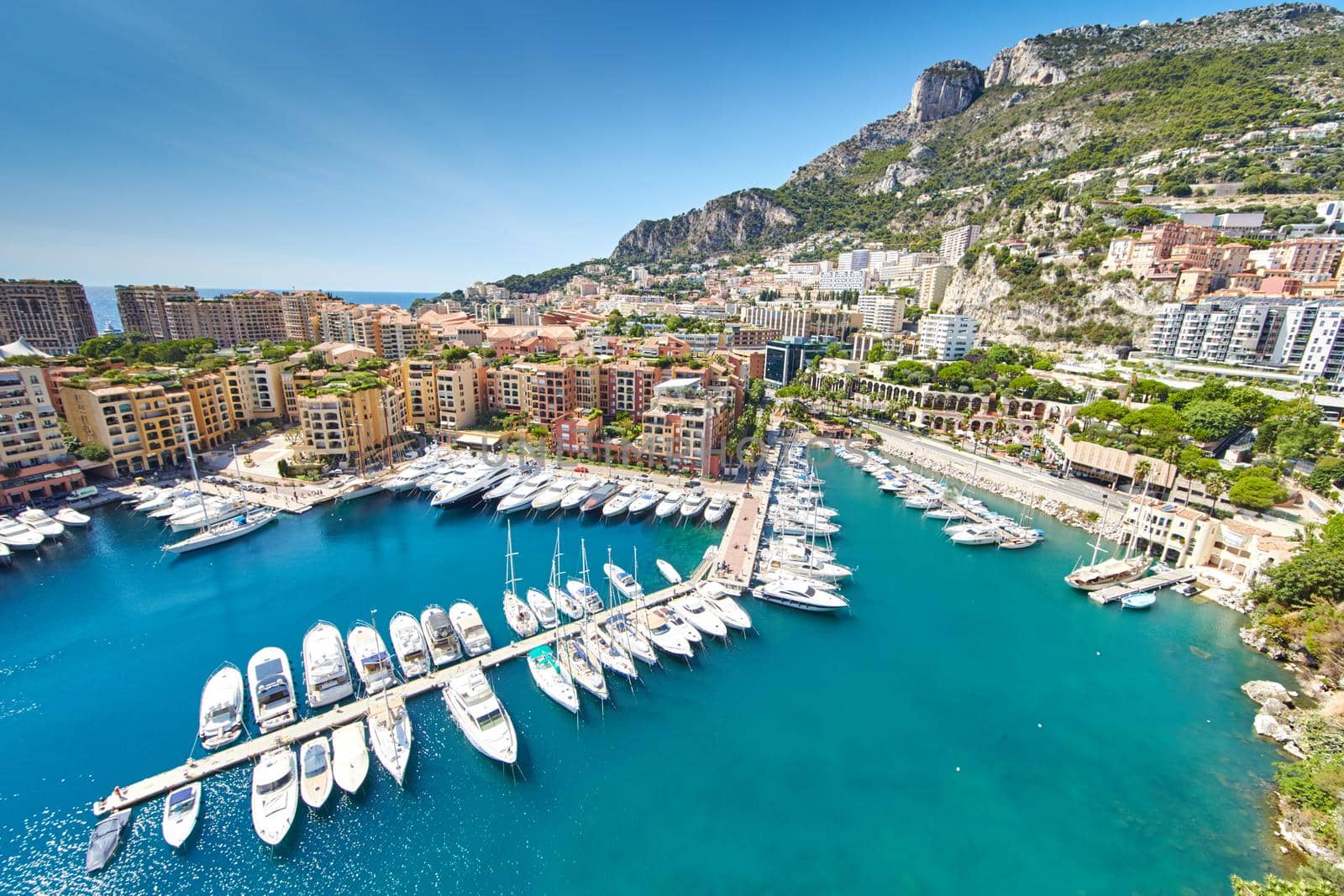 Panoramic image of Port Fontvieille - Monaco, top view from Monaco Ville, azur water, sun reflections on the water, harbour at sunny day, luxury apartments, a lot of yachts and boats, mountain. High quality photo