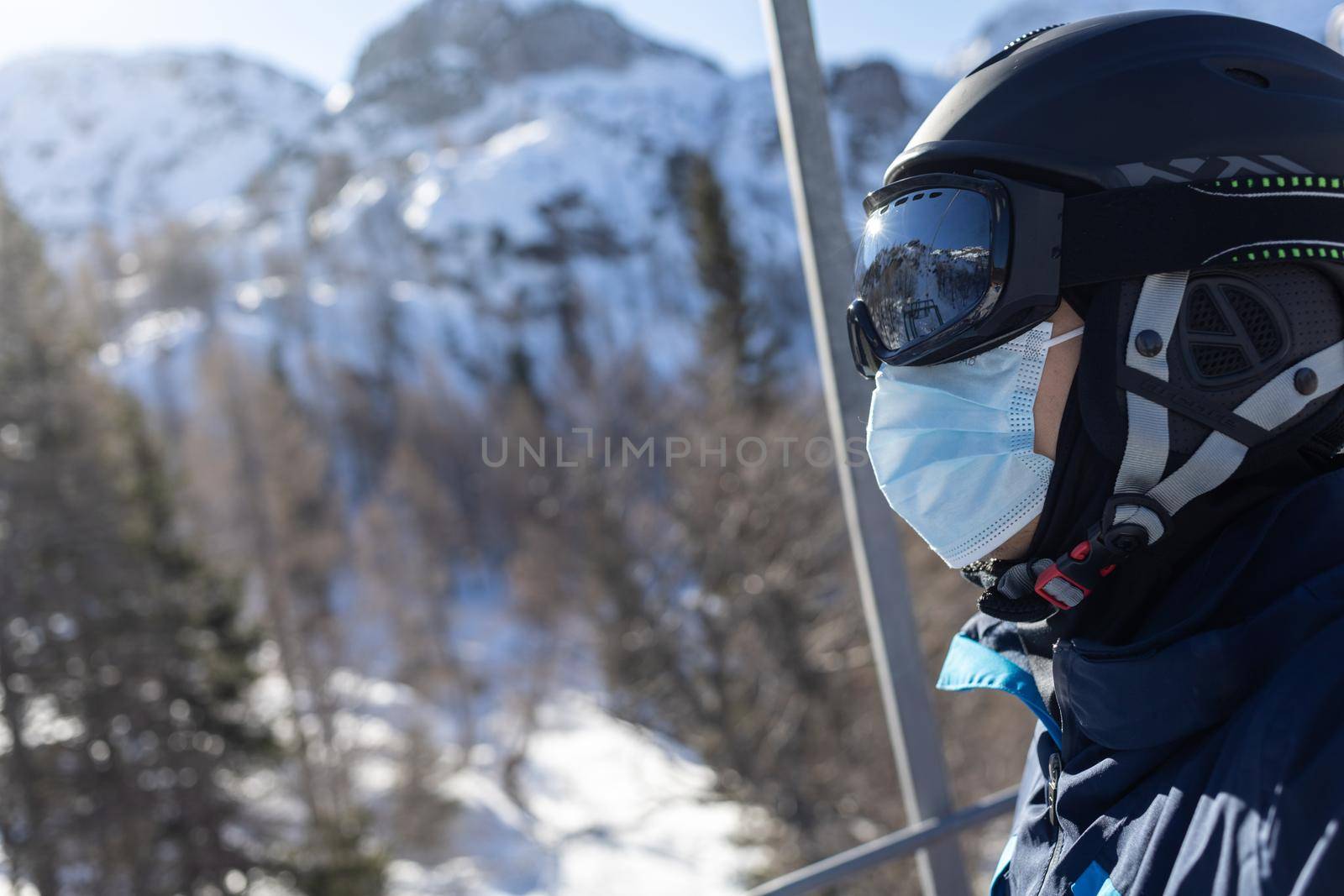 ski resort man on chairlift in helmet and medical mask by Chechotkin