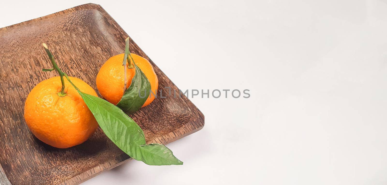 Two fresh ripe tangerines with leaves and branches on a dark square wooden plate, close-up, space for text on the right by claire_lucia