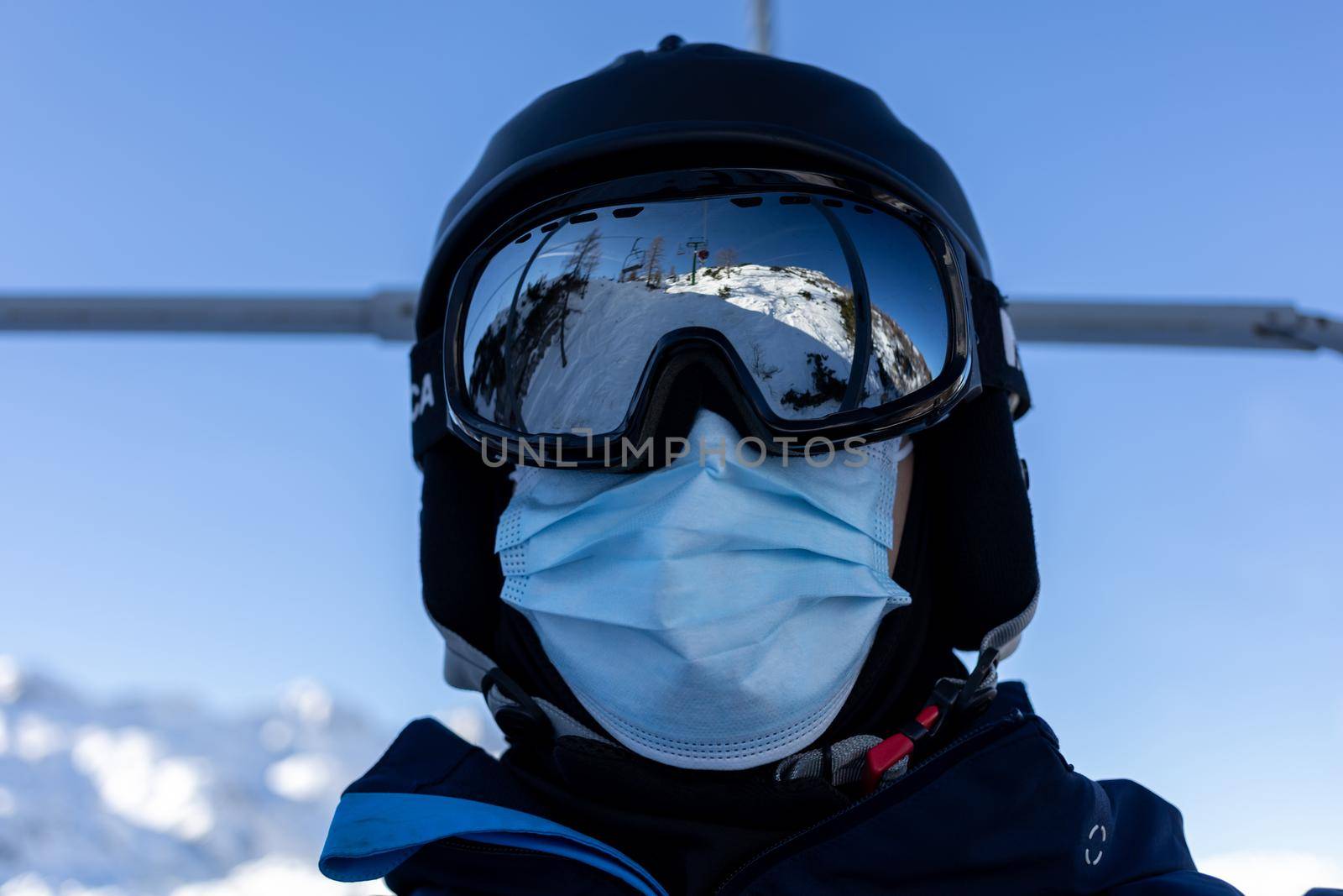 ski resort man on chairlift in helmet and medical mask by Chechotkin