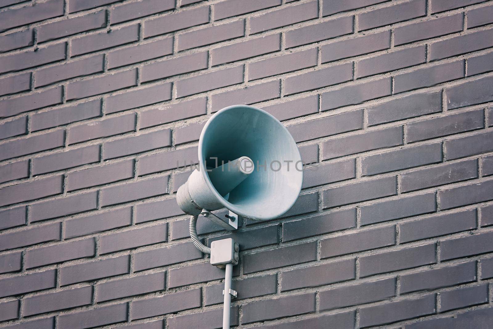 Loud speaker on brick wall. Megaphone hanging on building. City hazard warning system. Providing security in town, notification of emergencies.