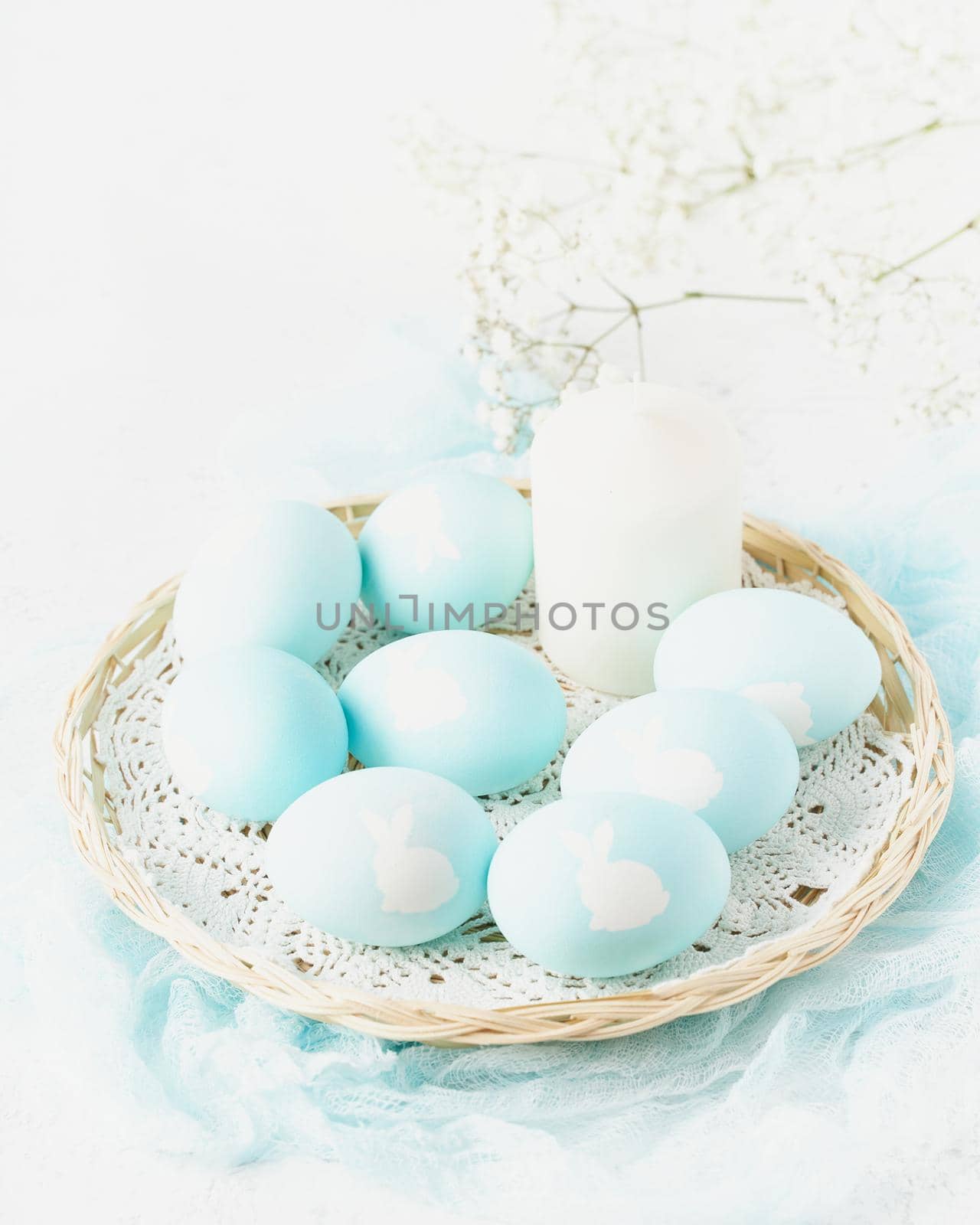 Easter. Holiday. Light white background, gentle pastel colors. Blue eggs with image of rabbit in basket. Flowers in background, side view, vertical