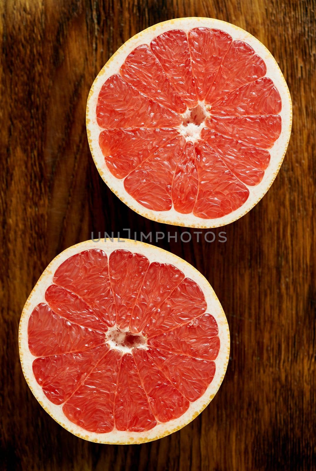 Two half of red grapefruit, bright circles on a dark wooden background. citrus fruits, vertical