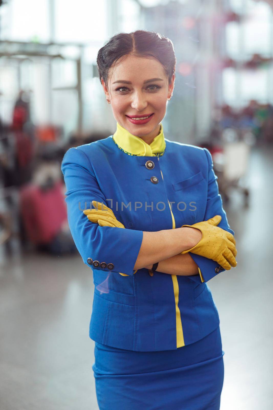 Cheerful flight attendant in air hostess uniform looking at camera and smiling while keeping arms crossed