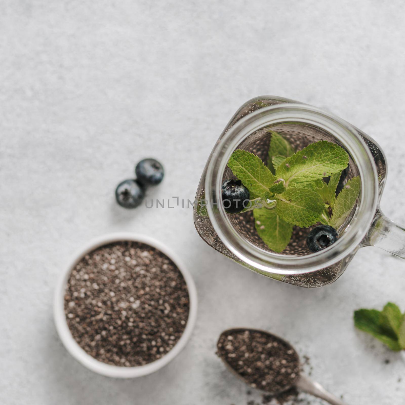 View from above chia water in mason jar with mint and blueberry on gray cement background.Chia infused detox water with berries.Copy space for text.Top view. Healthy eating, drinks, diet,detox concept