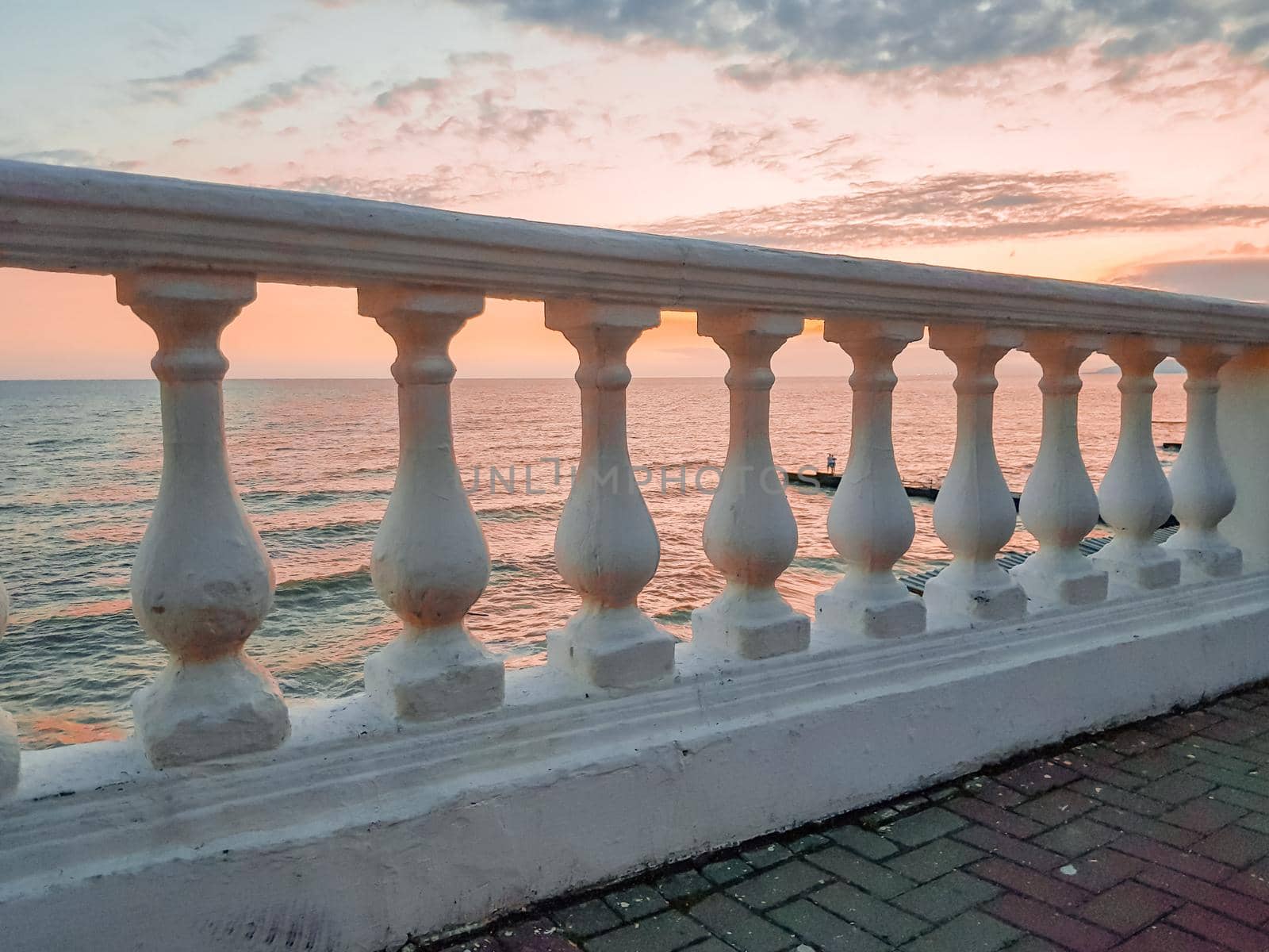 Classic white plaster balustrade on the background of a calm sea at sunset - a delicate pink mood.