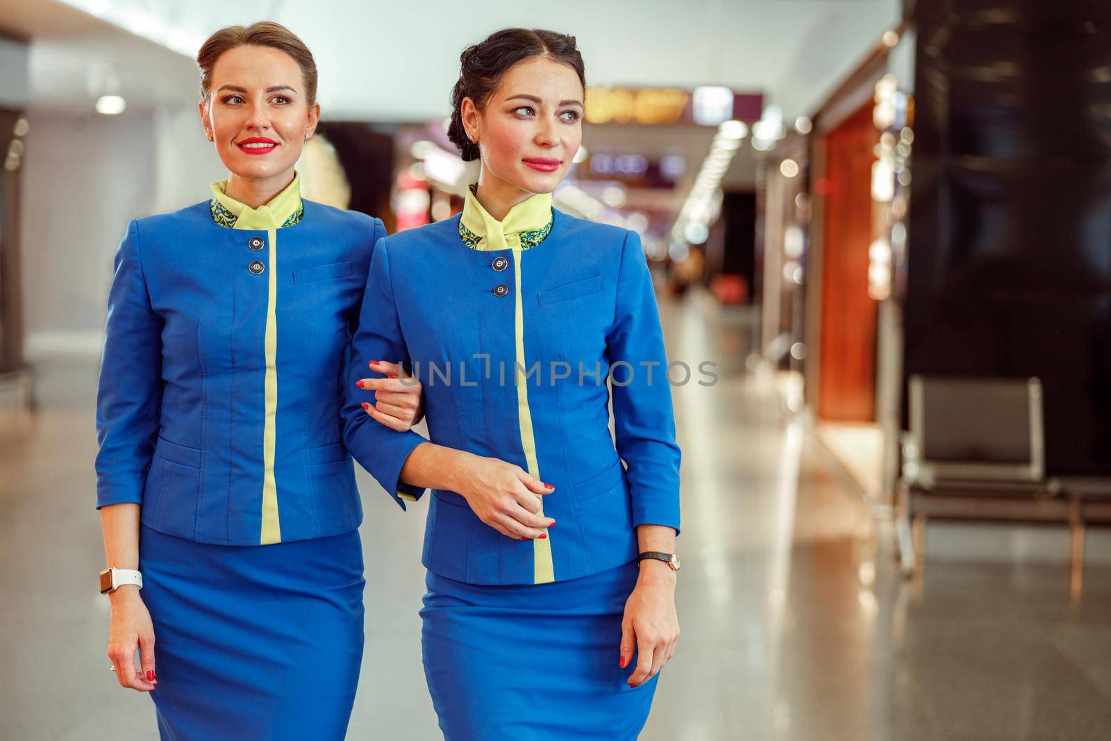 Woman stewardess in aviation air hostess uniform holding colleague hand and smiling while waiting for plane in airport terminal