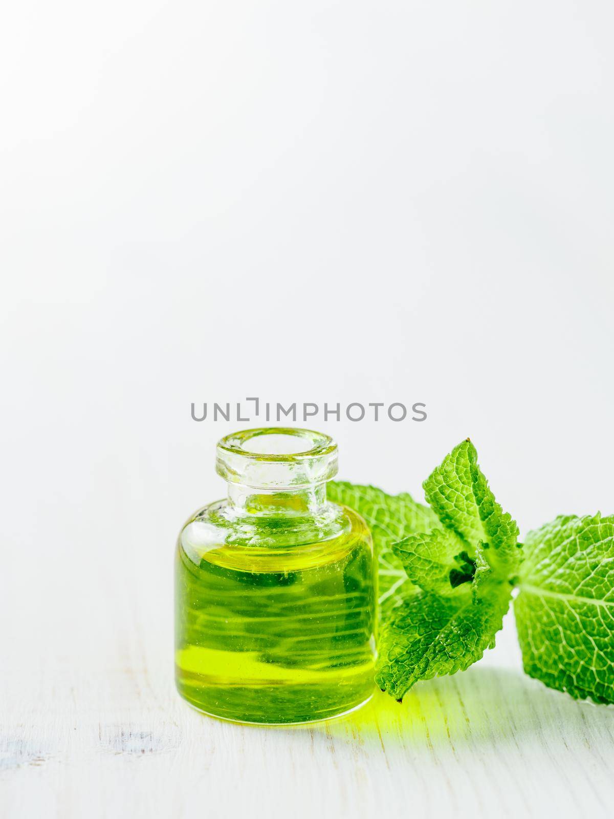 Organic essential mint oil or melissa oil with green leaves of mint. Mint melissa oil on white tabletop with copy space. Vertical