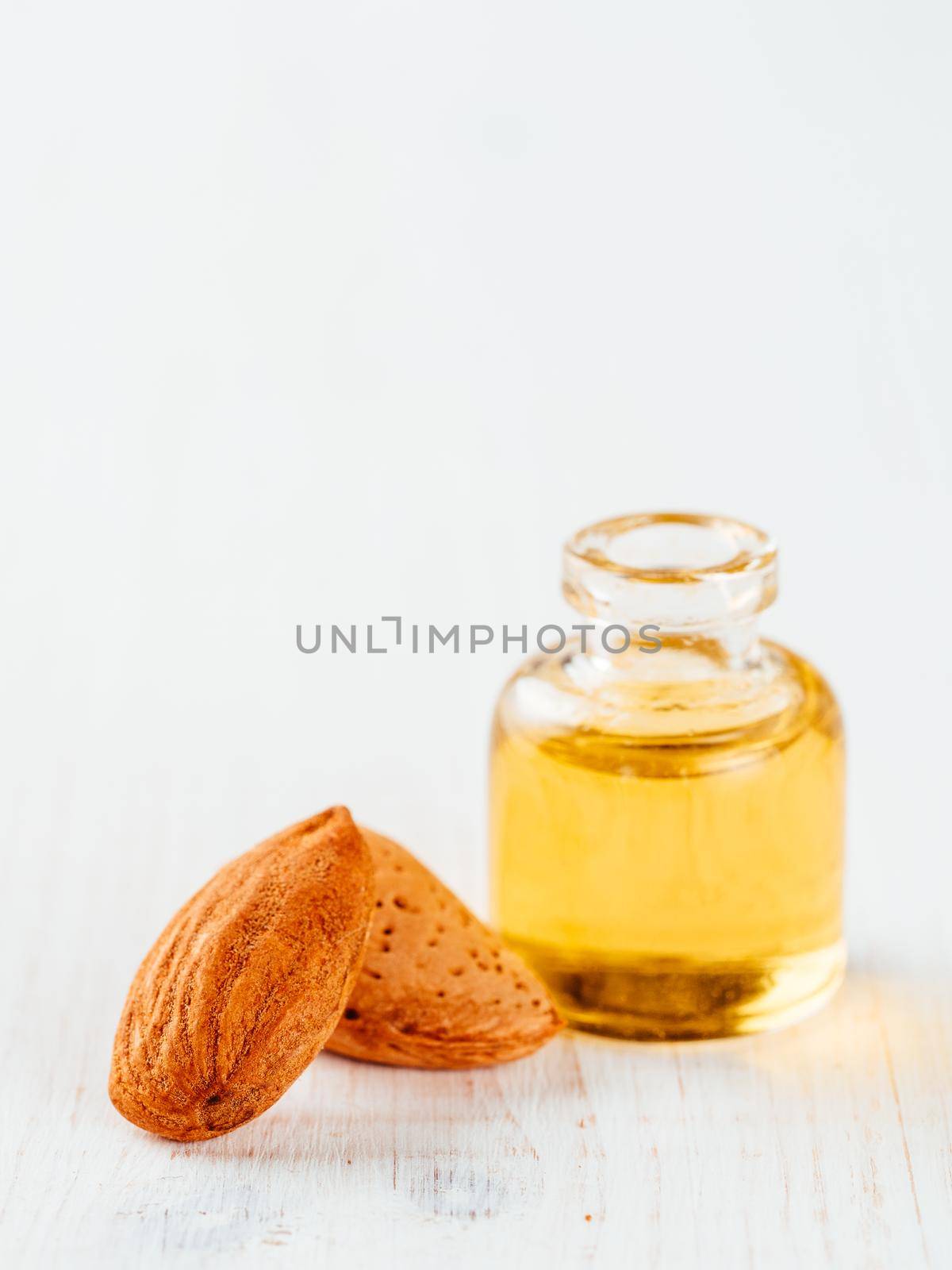 Small glass bottle of almond oil and almonds on white wooden tabletop with copy space. Vertical