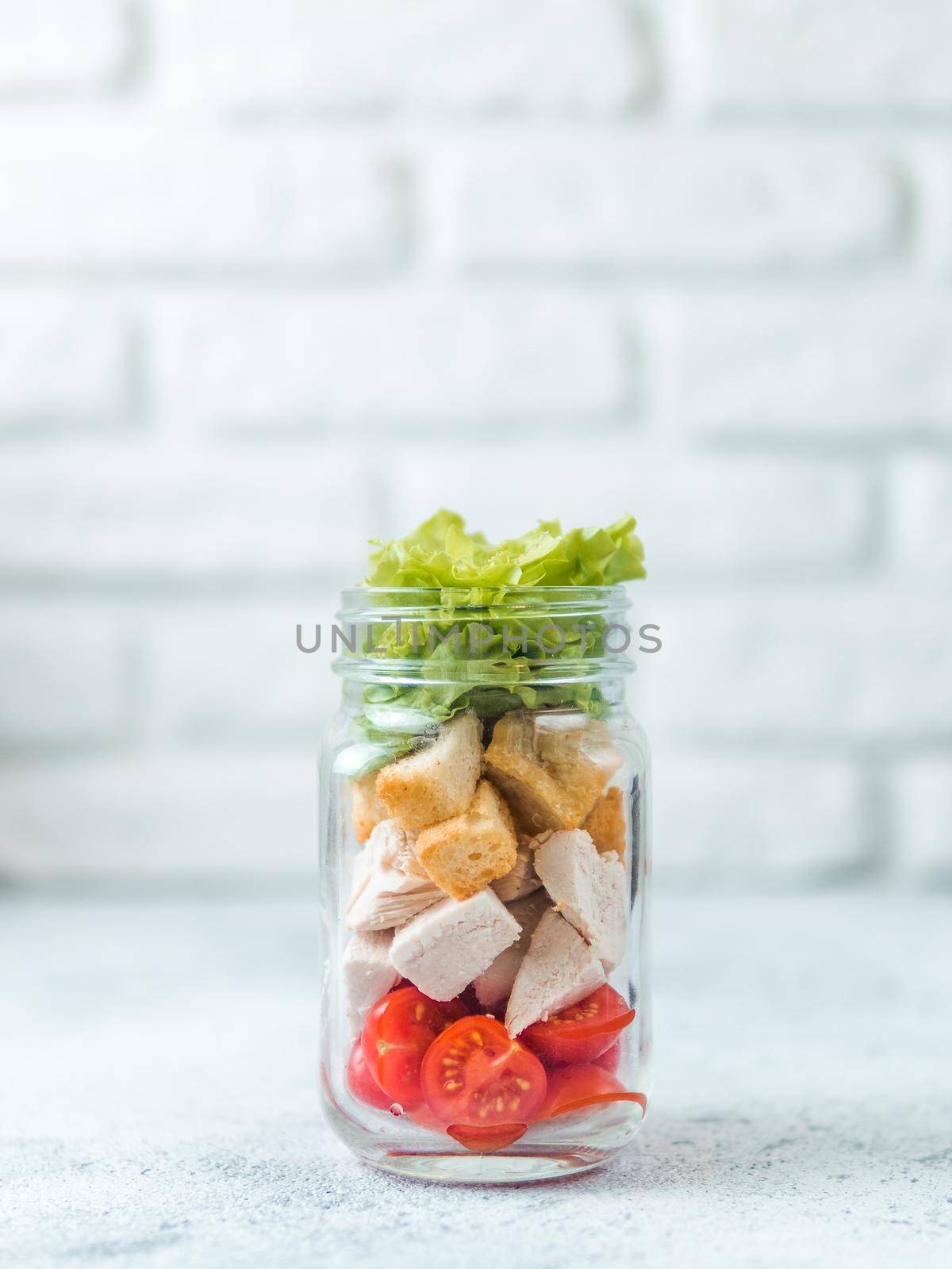 Caesar salad in glass mason jar on gray background. Copy space for text. Homemade healthy caesar salad layered in jar. Healthy food, trendy modern food, diet concept, idea, recipe. Vertical.