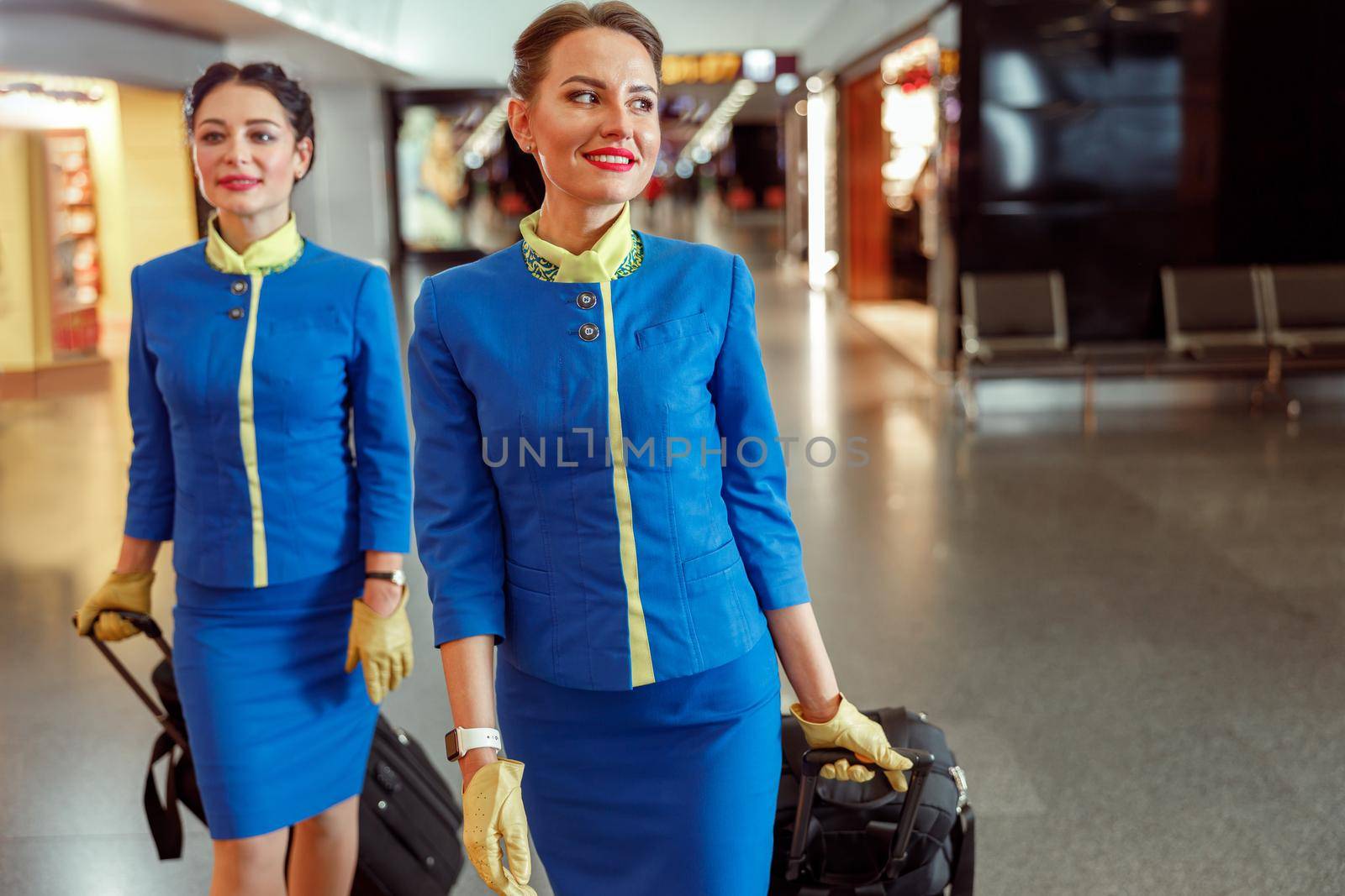 Cheerful women stewardesses carrying travel bags at airport by Yaroslav_astakhov