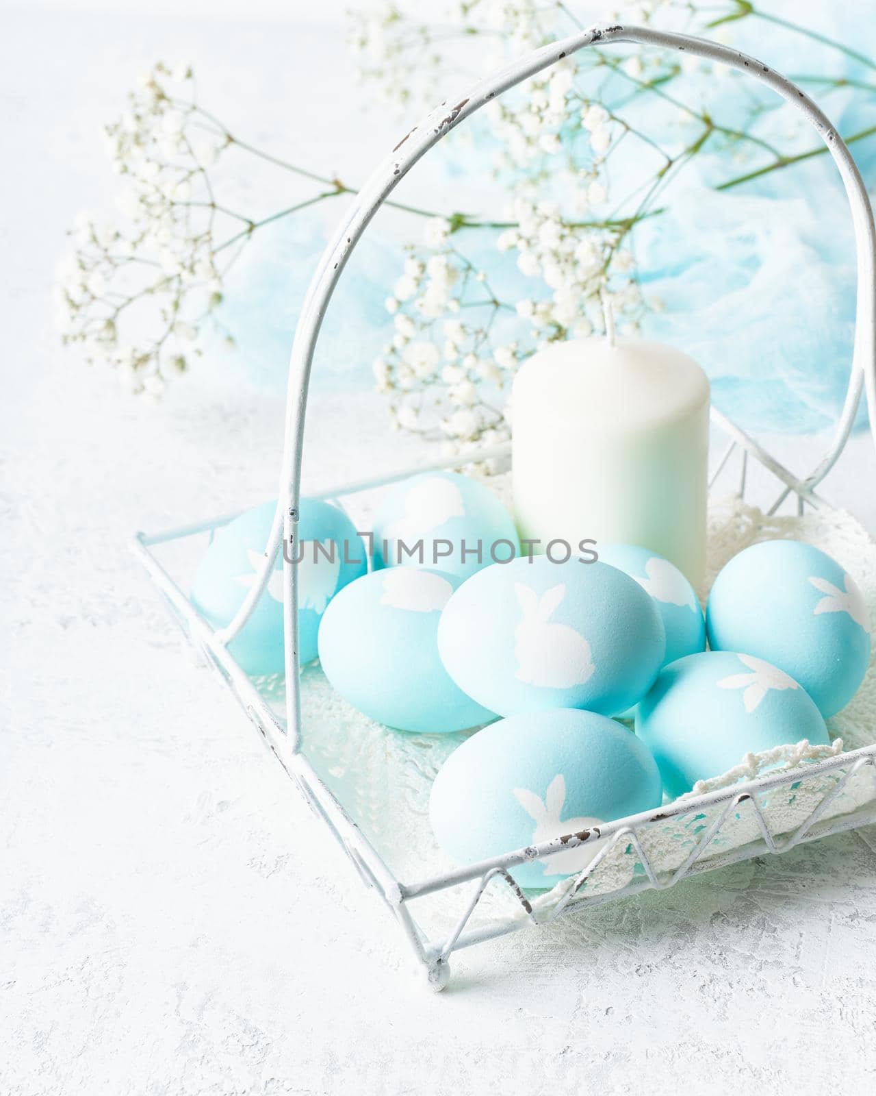 Easter. Holiday. Light white background, gentle pastel colors. Blue eggs with image of rabbit in basket. Flowers in background. Side view, vertical