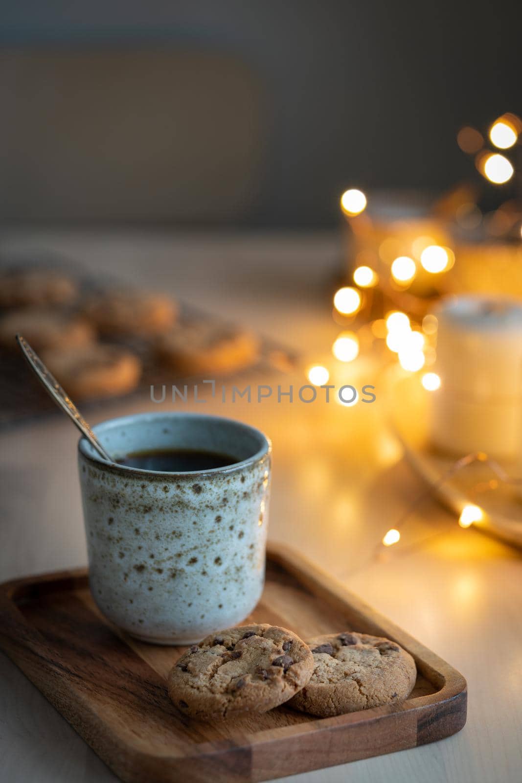 Cozy evening, mug of drink, holiday decorations, candles and lights garlands. Christmas background with Chocolate chip cookies, cup of tea. Still life vertical photo