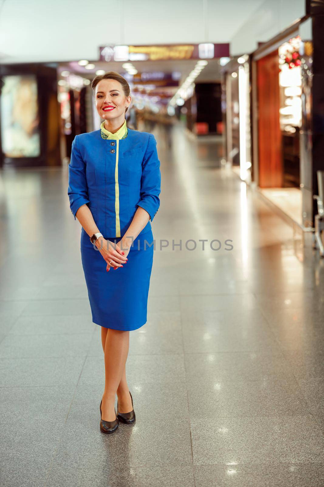 Full length of joyful female flight attendant in aviation air hostess uniform looking at camera and smiling