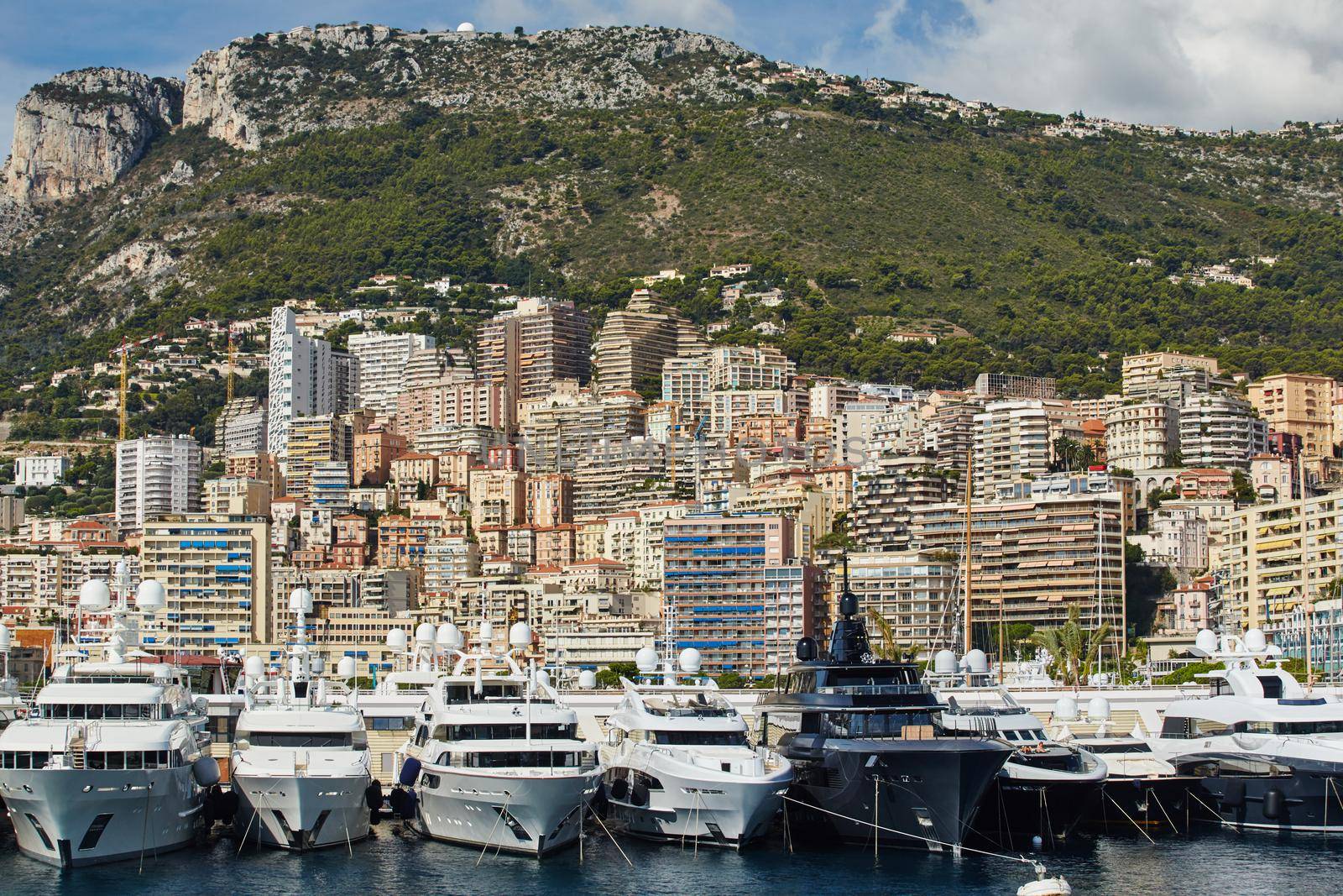 Monaco, Monte-Carlo, a lot of large motor yachts are parked side by side in the port, with huge fenders between them to avoid collision at sunny day, mooring ropes go into the azure water. High quality photo