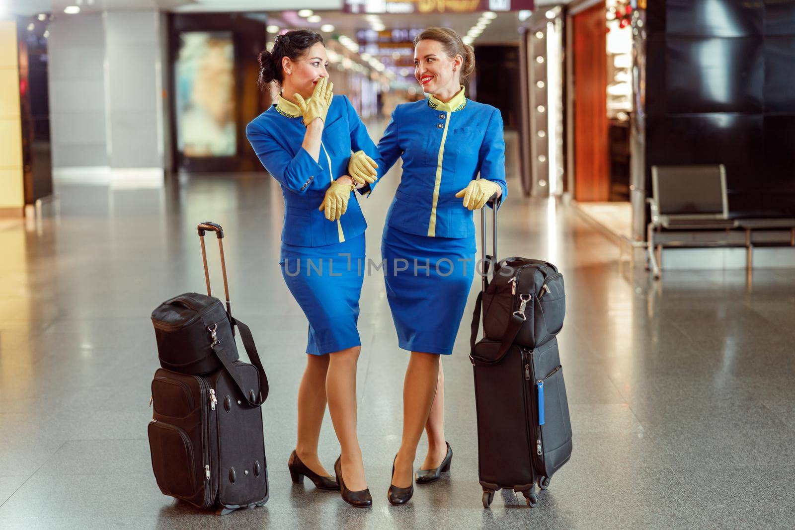 Joyful stewardesses with travel bags standing in airport terminal by Yaroslav_astakhov