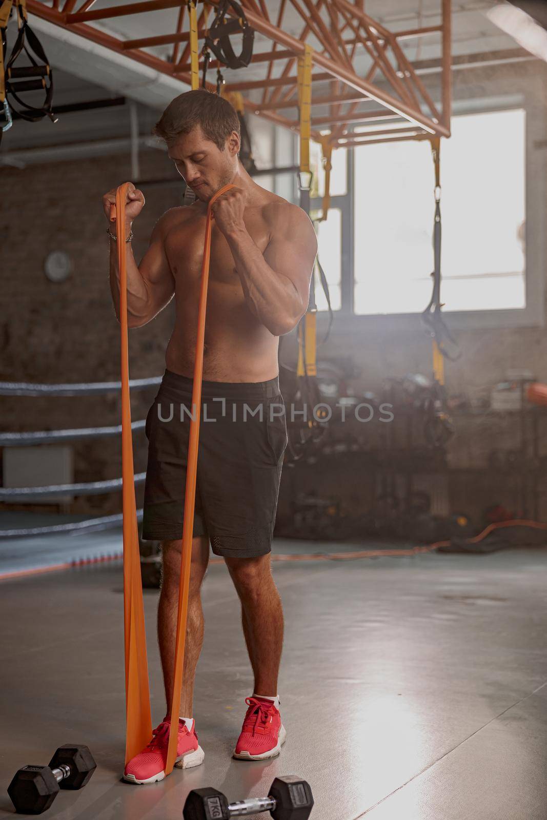 Fully concentrated athletic man performing exercises using resistance band during training in sports club
