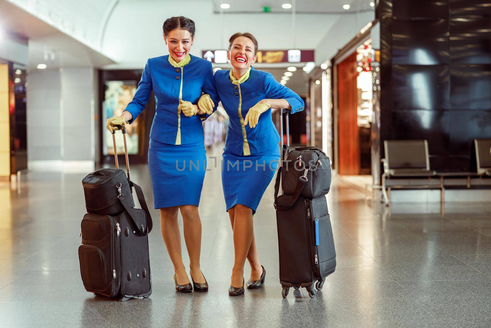 Cheerful stewardesses with travel bags standing in airport terminal by Yaroslav_astakhov