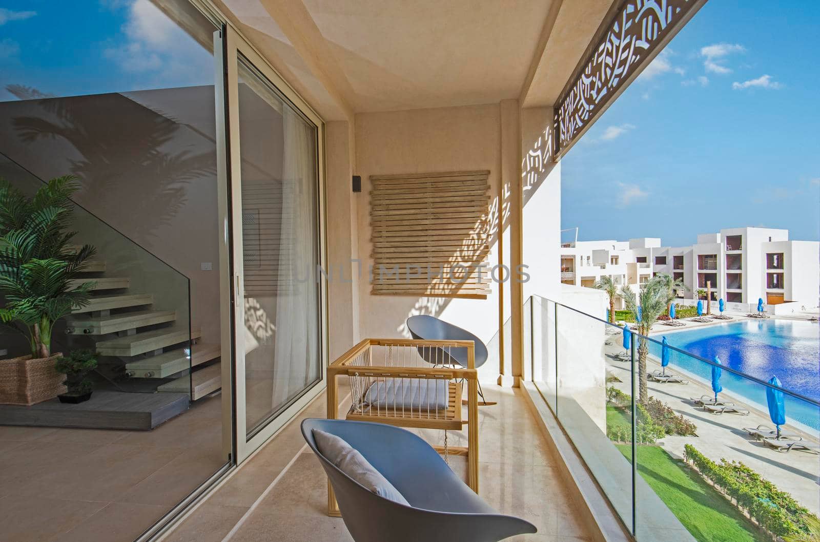 Terrace furniture of a luxury apartment in tropical resort with table and chairs on balcony over swimming pool view