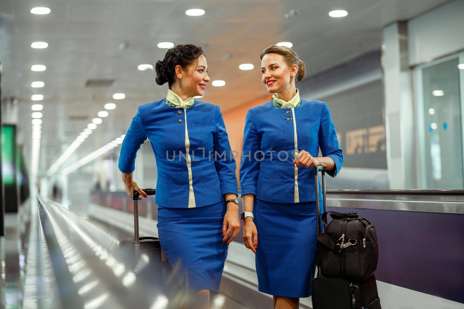 Cheerful stewardess with travel bags standing in airport terminal by Yaroslav_astakhov