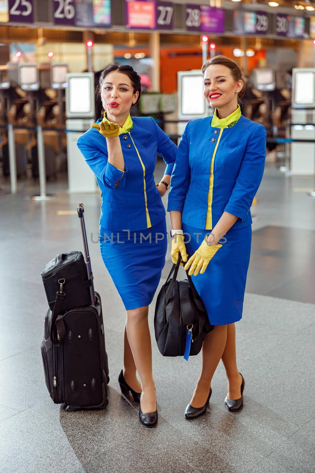 Stewardesses with travel bags standing in airport terminal by Yaroslav_astakhov