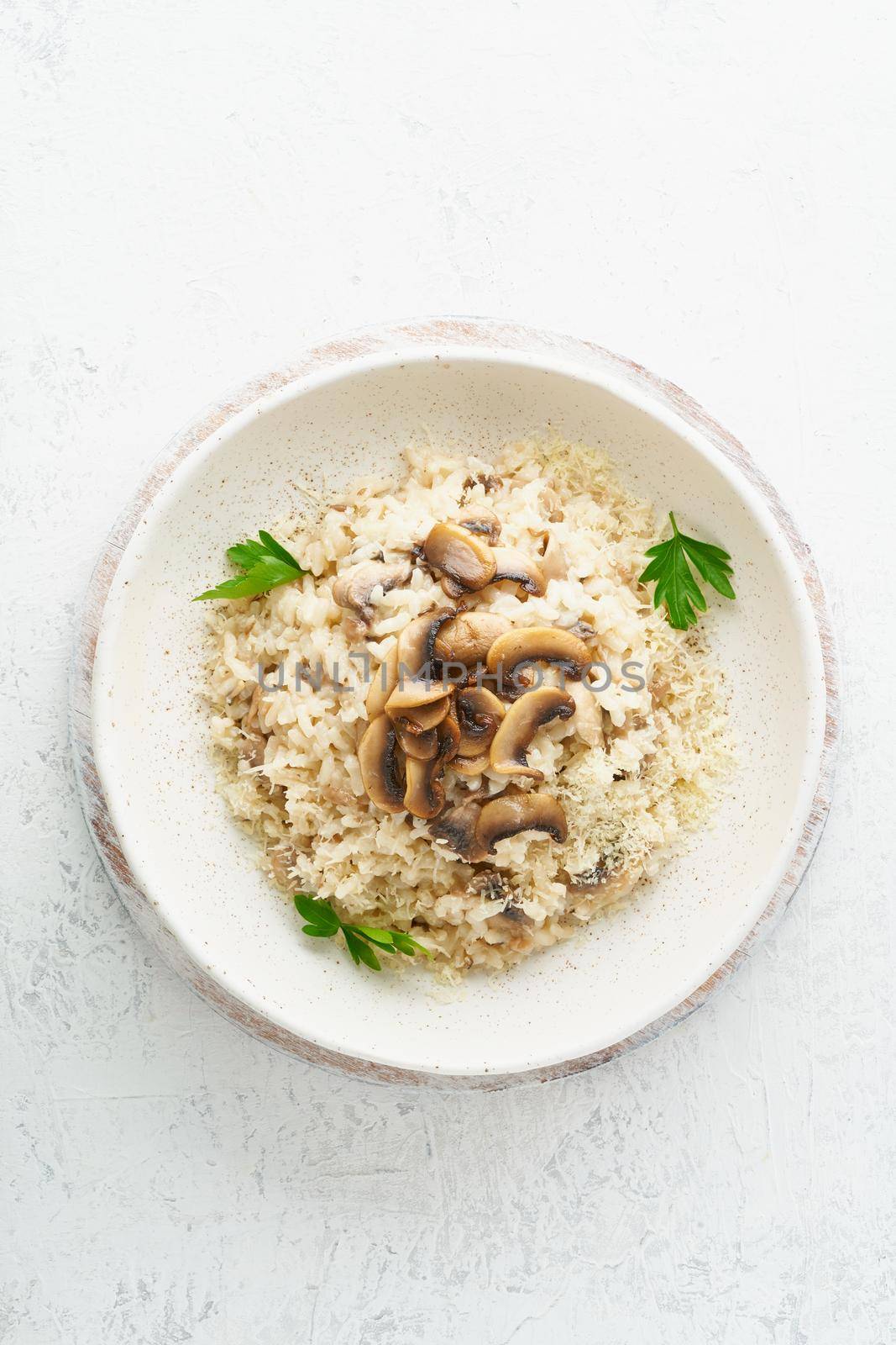 Risotto with mushrooms in plate. Rice porridge with mushrooms and parsley. White table, spoons, mushrooms. Hot dish, italian cuisine, top view, vertical, copy space
