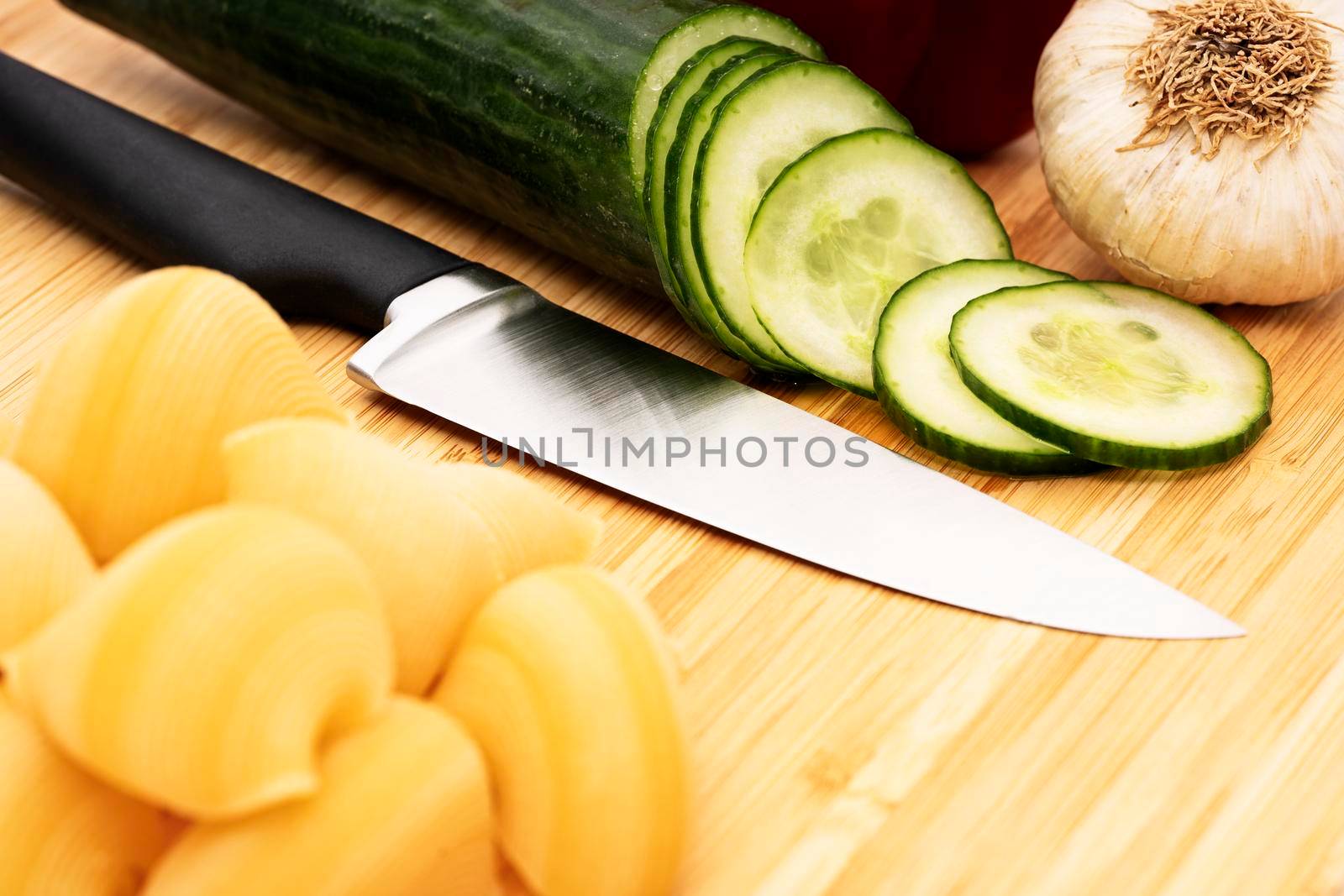 Chopped cucumber on wooden cutting board with knife by Mendelex
