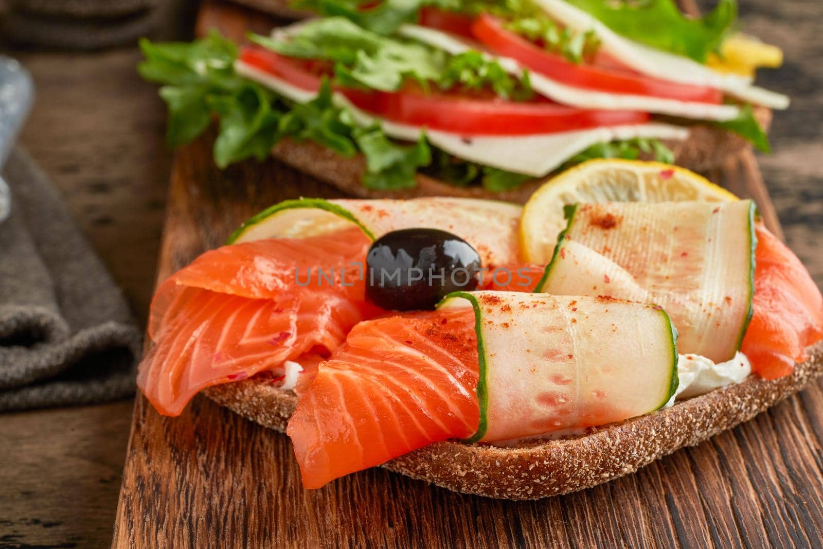 Smorrebrod - traditional Danish sandwiches. Black rye bread with salmon, cream cheese, cucumber and olives on dark brown wooden background