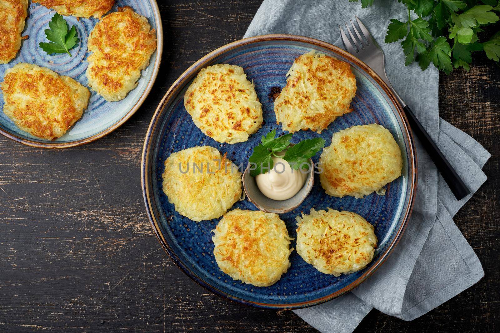 Hashbrown, hash brown potatoes fried pancakes, traditional american cuisine. Crispy hashed browned potatoes in blue plate on dark brown table, top view.