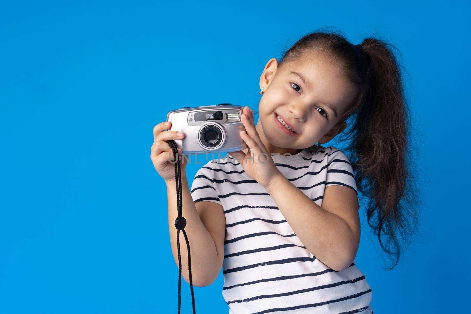 Portrait of a little girl with camera against blue background, close up