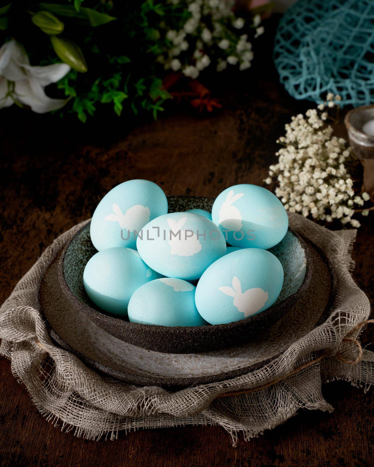 Unusual Easter on dark old background. Ceramic brown bowl with blue eggs. Darkness, rays of sunlight shine on eggs. Concept of new life, rebirth. Rustic style. Vertical, copy space