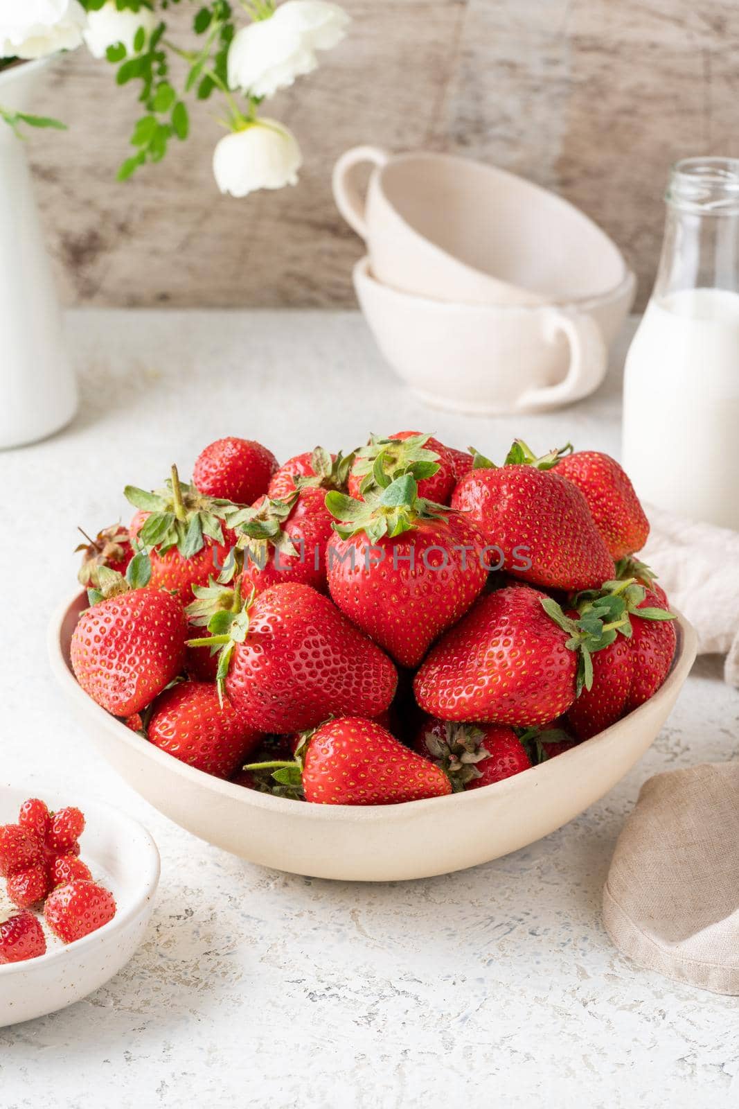 Bowl with strawberry on white table, bottle with milk, flower. Still-life photo with summer berries by NataBene