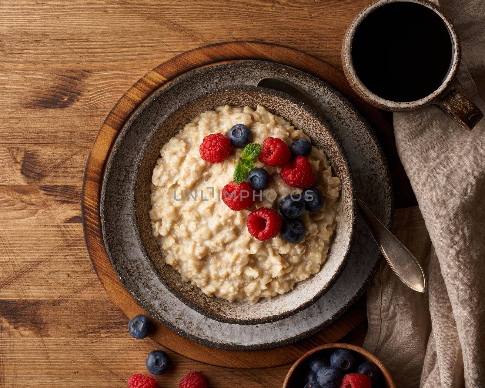 Oatmeal rustic porridge with blueberry, raspberries in ceramic vintage bowl, dash diet with berries, wooden dark brown background, top view close up. Healthy diet breakfast