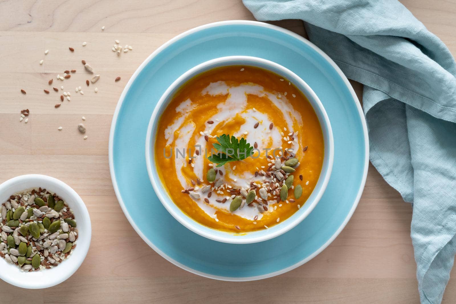Pumpkin soup with coconut milk and seeds in blue bowl, vegetarian healthy dieting food on wooden background, top view, copy space