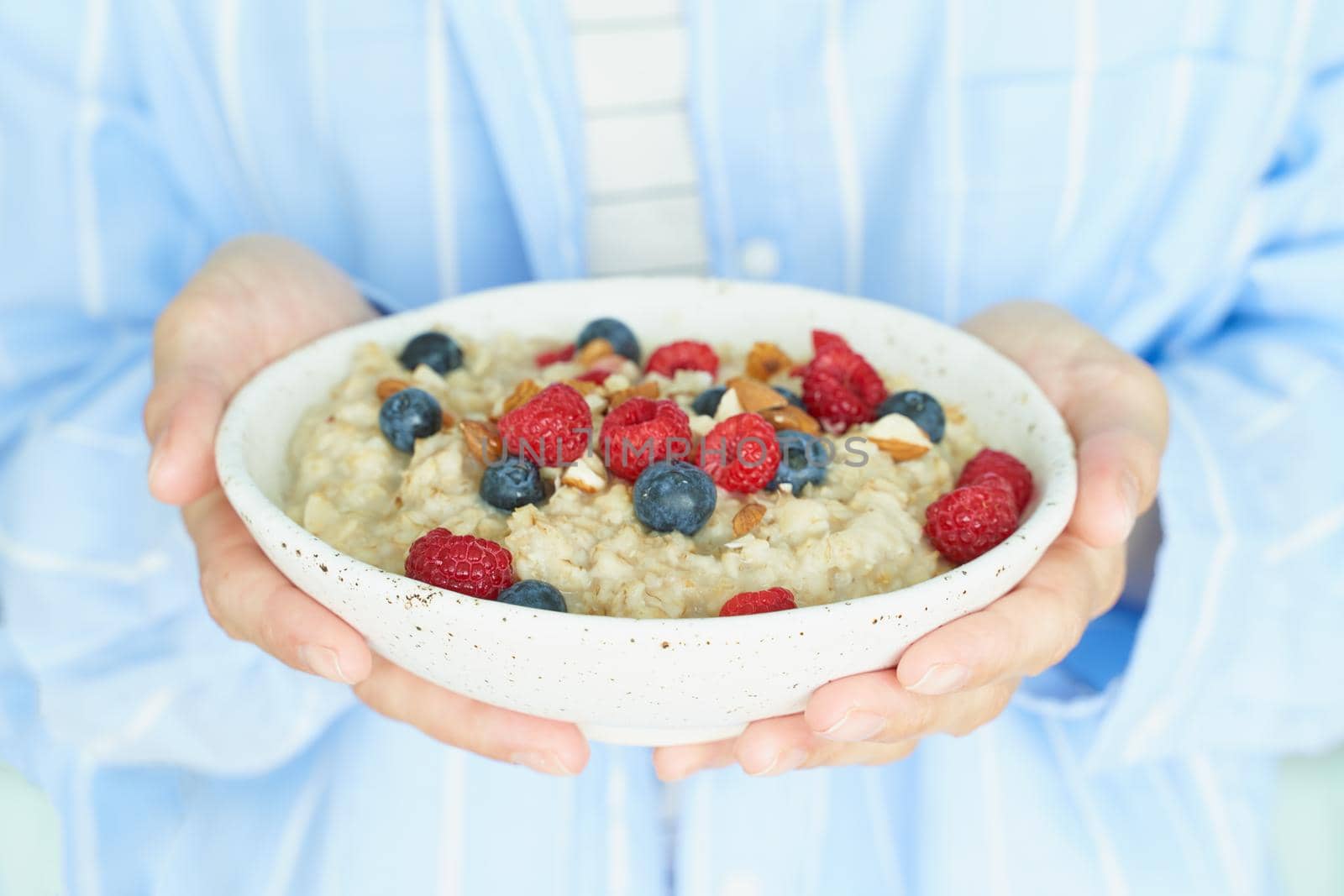 Faceless woman holds in hands breakfast, oatmeal porridge with berries and nuts by NataBene