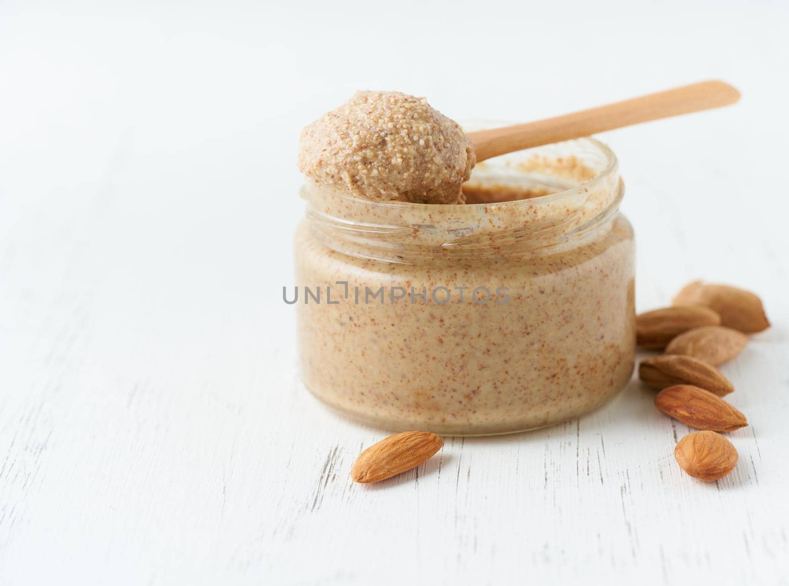 Almond butter, raw food paste made from grinding almonds, glass jar, side view, close up by NataBene