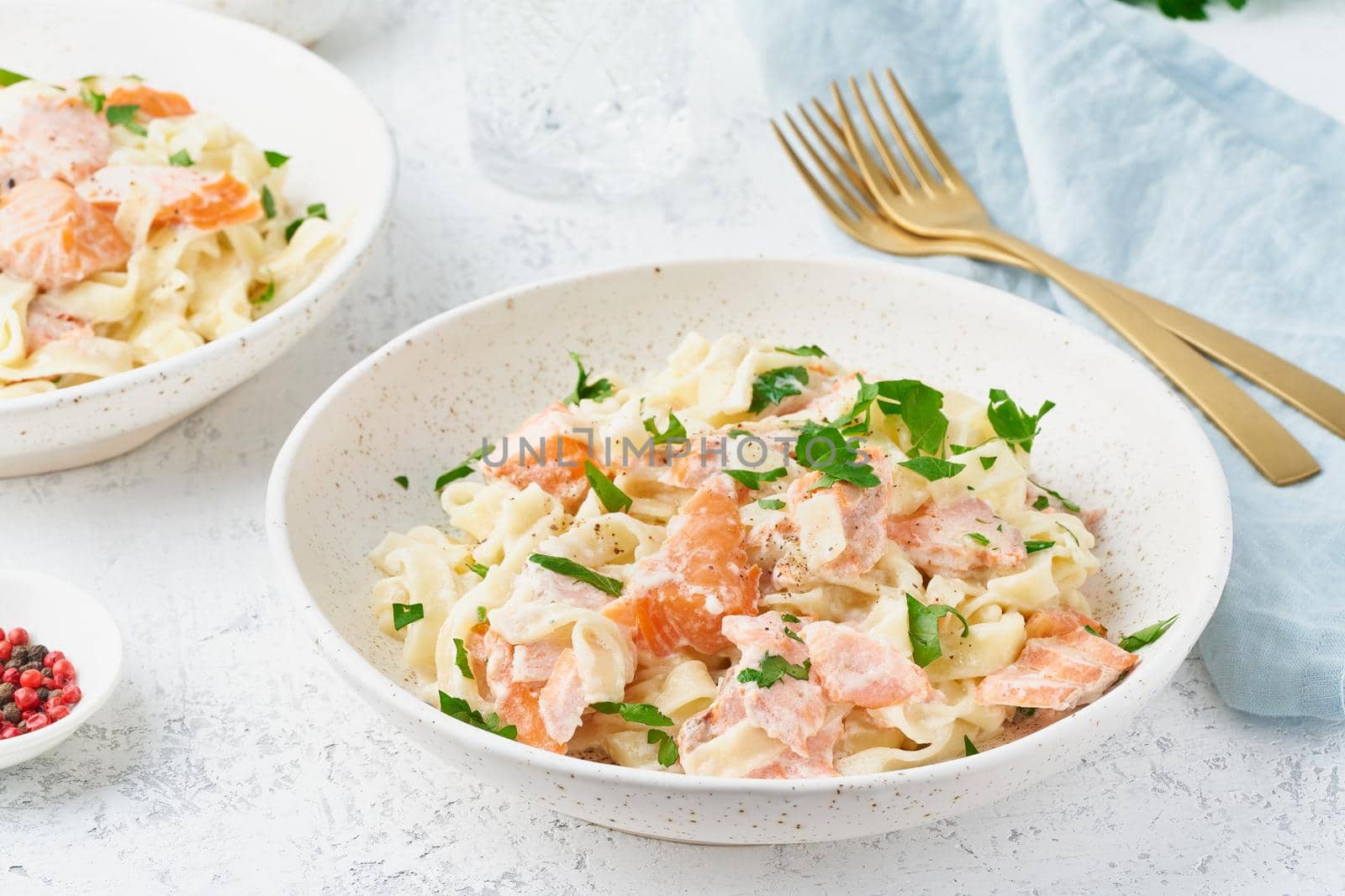 Salmon pasta, tagliatelle with fish and creamy sauce. Italian dinner with seafood for two at table. White background, side view