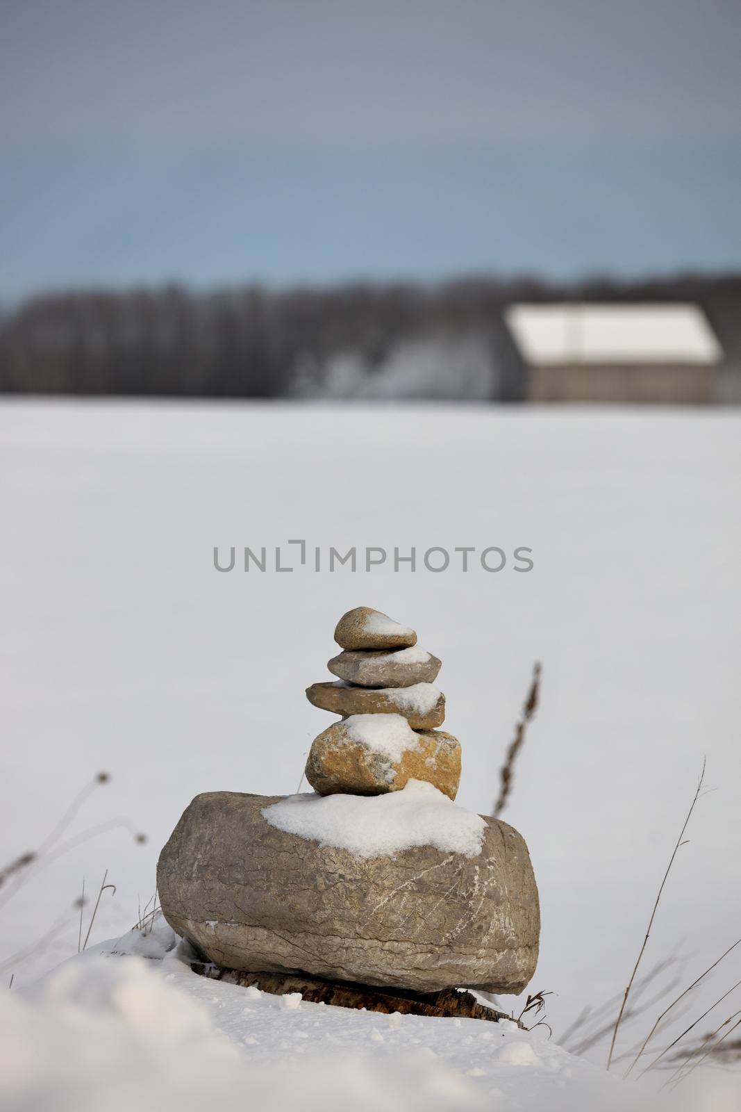 An Inukshuk in a field in the winter with a barn in the distant background. High quality photo