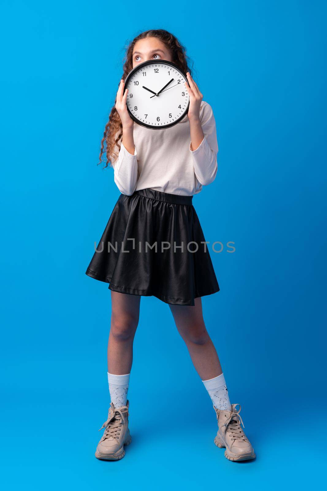 Beautiful teen girl holding wall clock over blue background, close up