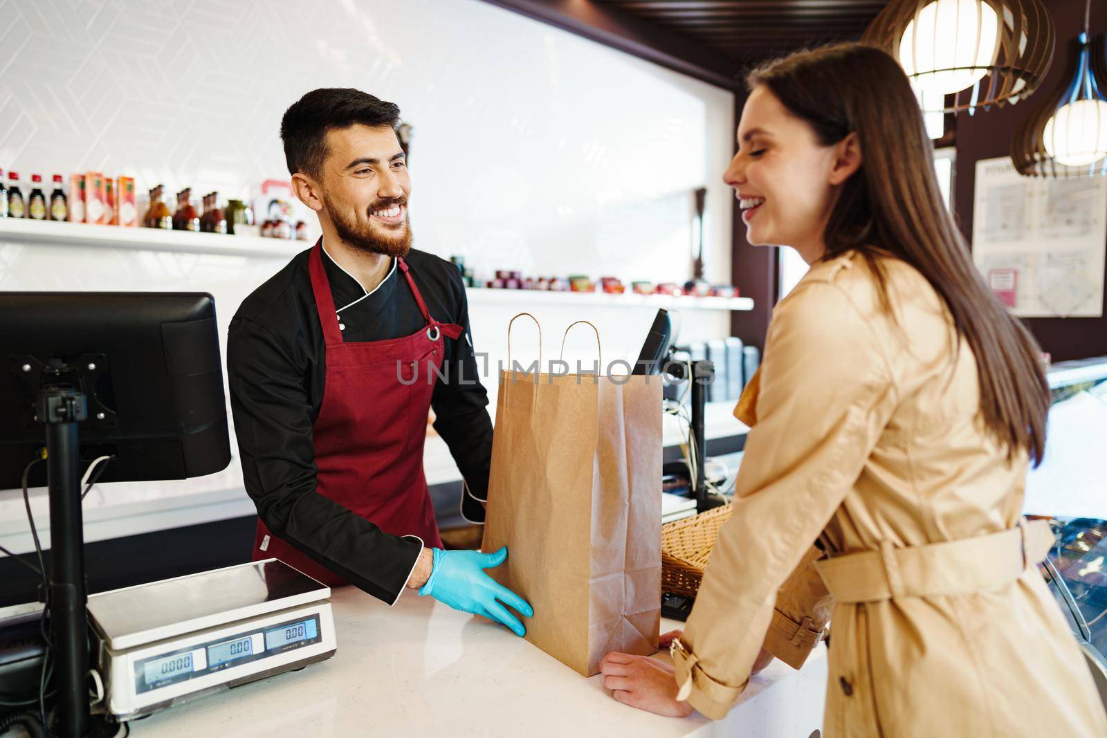 Shop assistant handling shopping bag to female customer in grocery store, close up