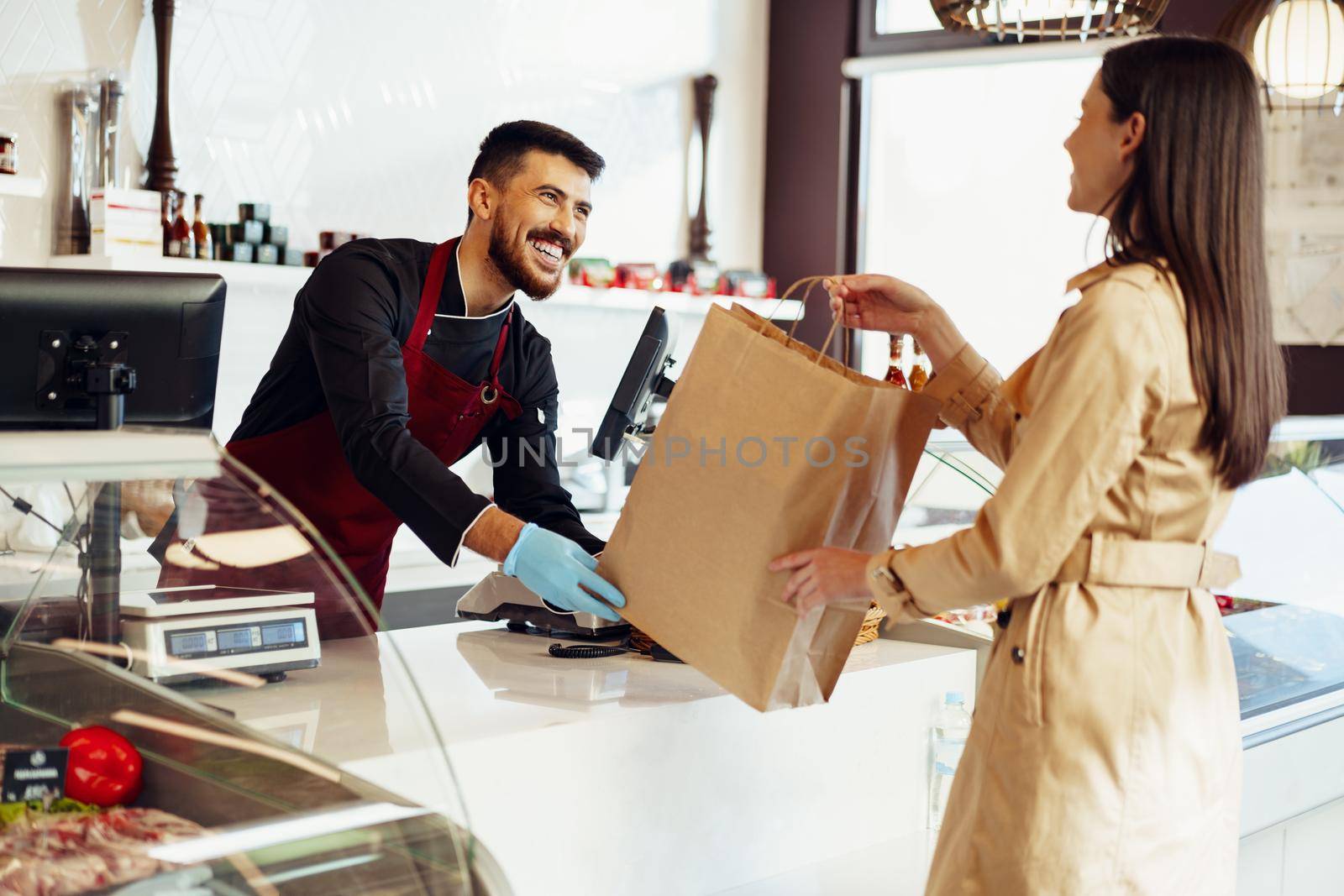 Shop assistant handling shopping bag to female customer in grocery store, close up