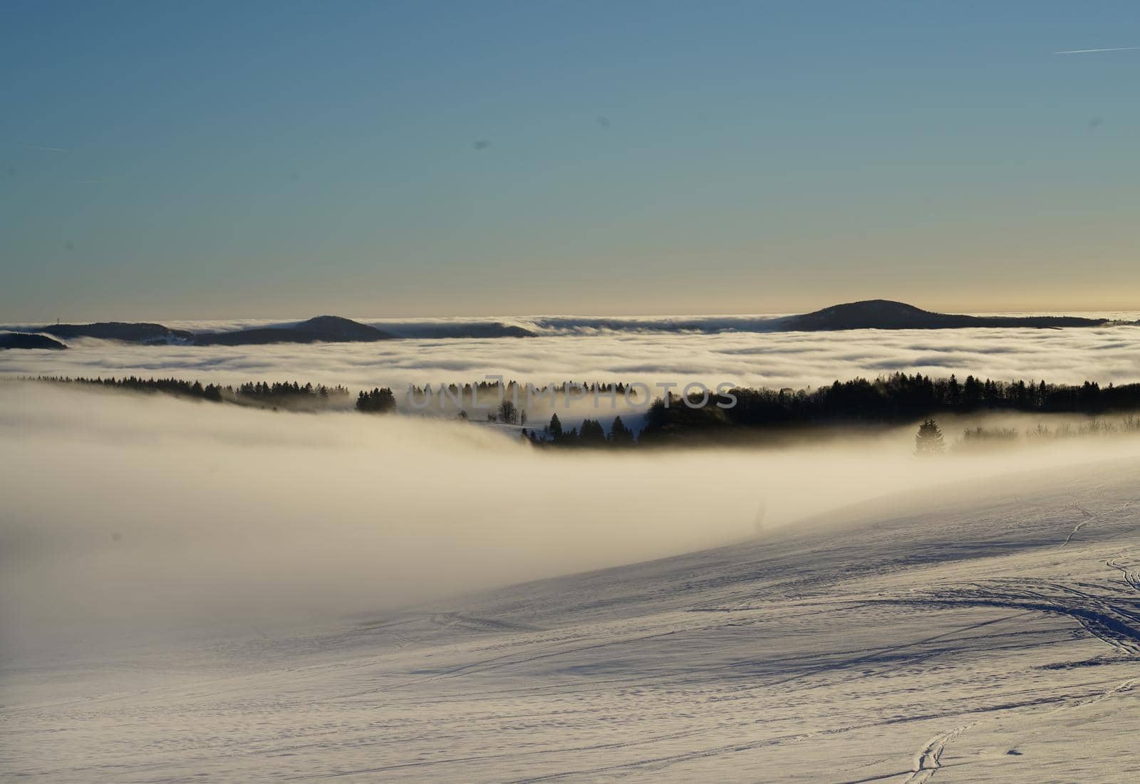 The concept of relaxing in the mountains in winter in the snow on skis, snowboards or sleds, walking under the setting sun at sunset on the Wasserkuppe mountain in Hesse Germany by Costin