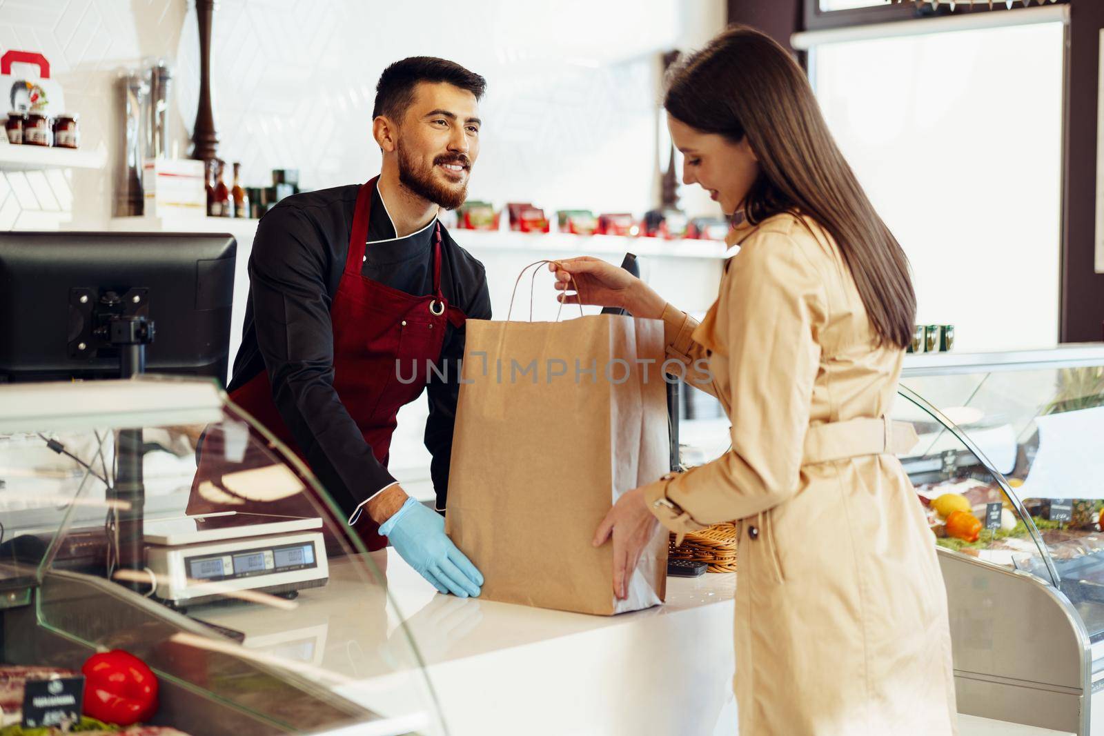 Shop assistant handling shopping bag to female customer in grocery store, close up