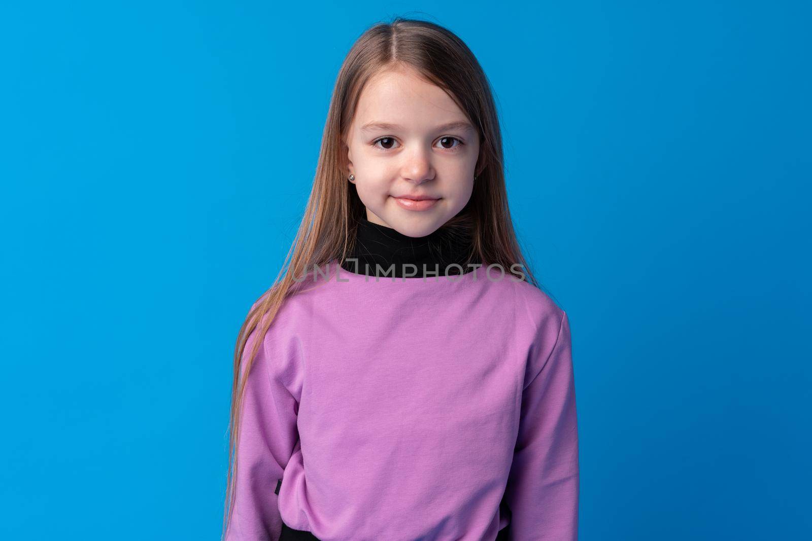 Portrait of a little smiling girl preteen on blue background, close up