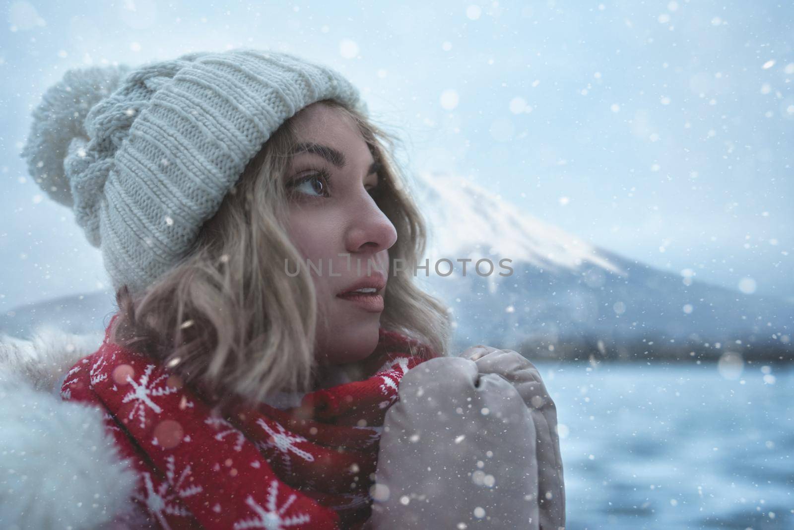 Portrait of Charming Woman at Ski Resort stands on the shore of a frozen lake, snowflakes falling on her face, a cold wind blows away, she is smiling. by Nickstock
