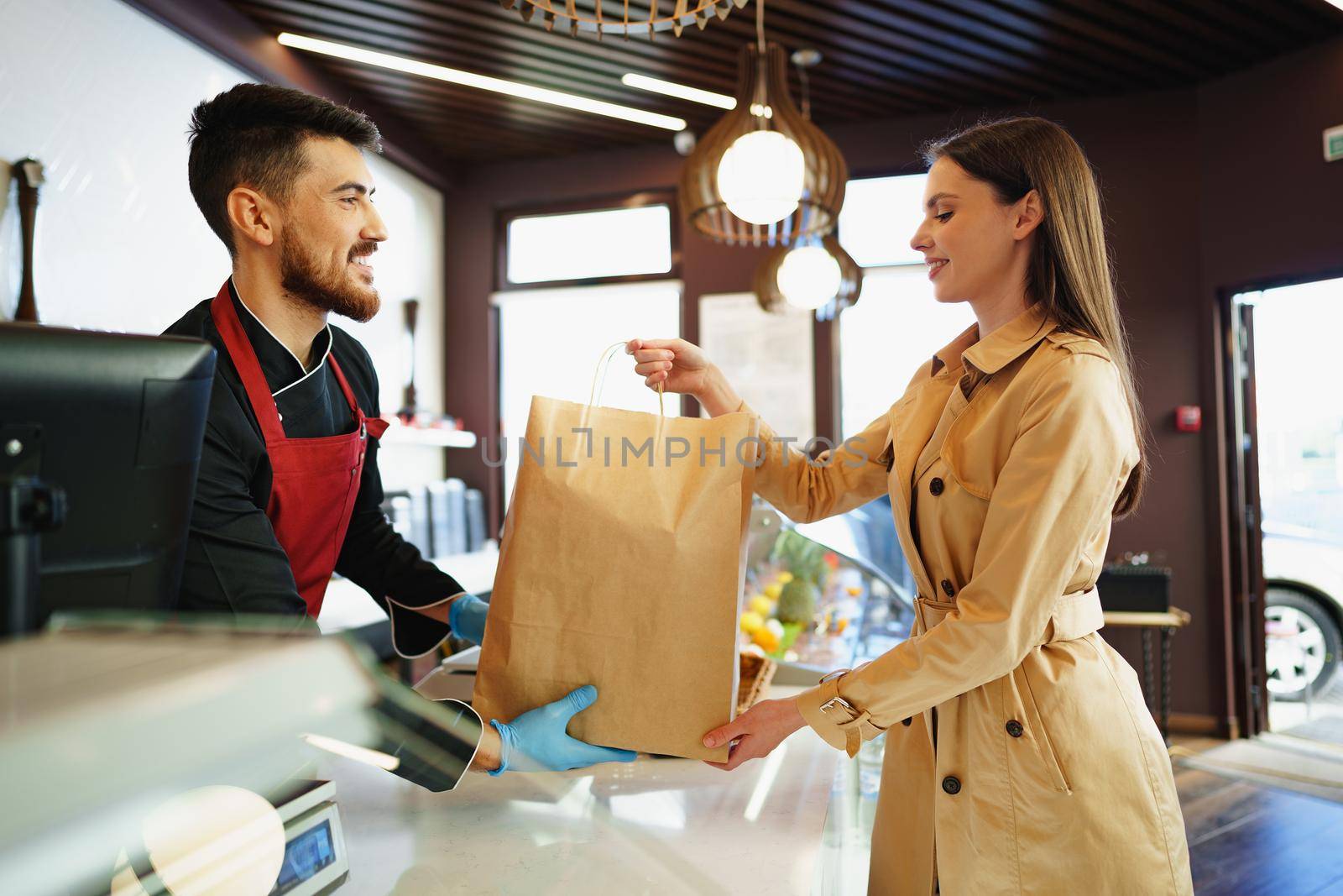 Shop assistant handling shopping bag to female customer in grocery store, close up