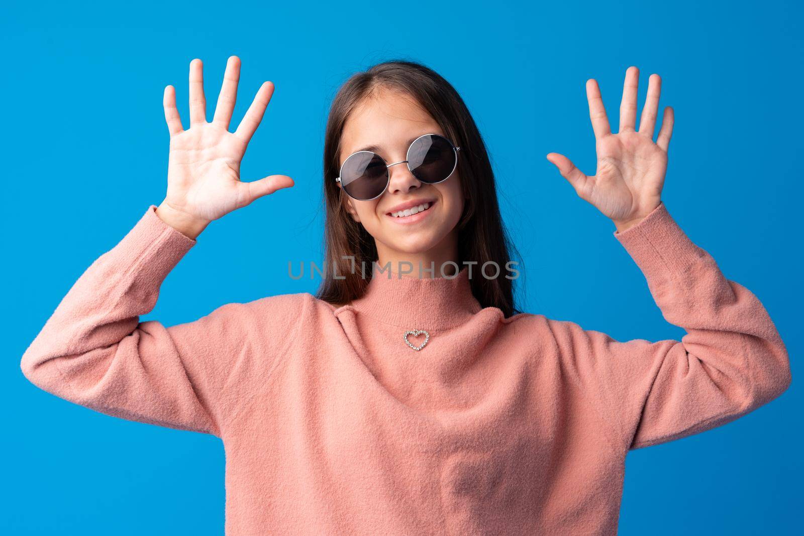 Little fashion girl in sunglasses against blue background, close up