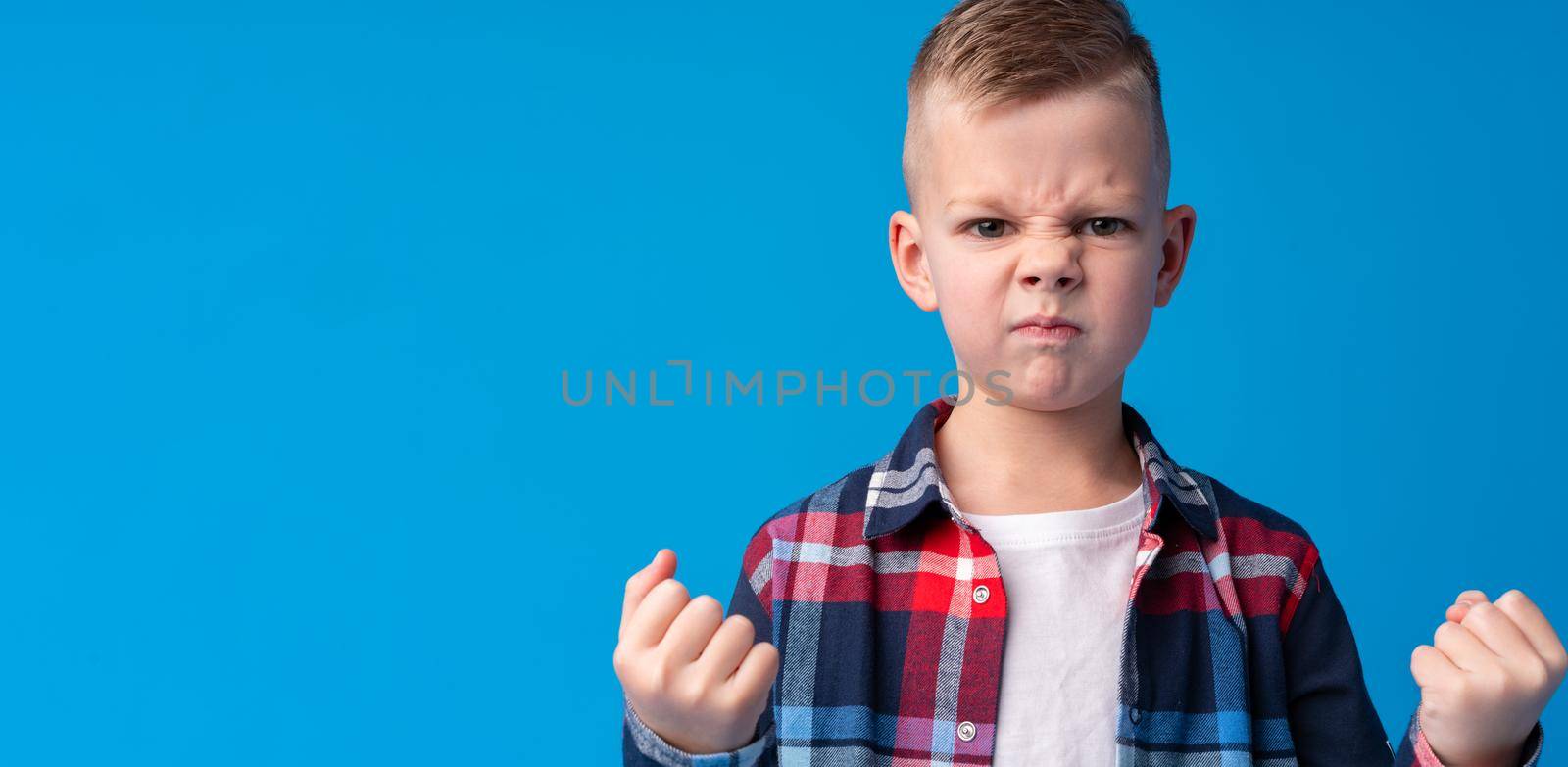Portrait of angry little boy on blue background, close up
