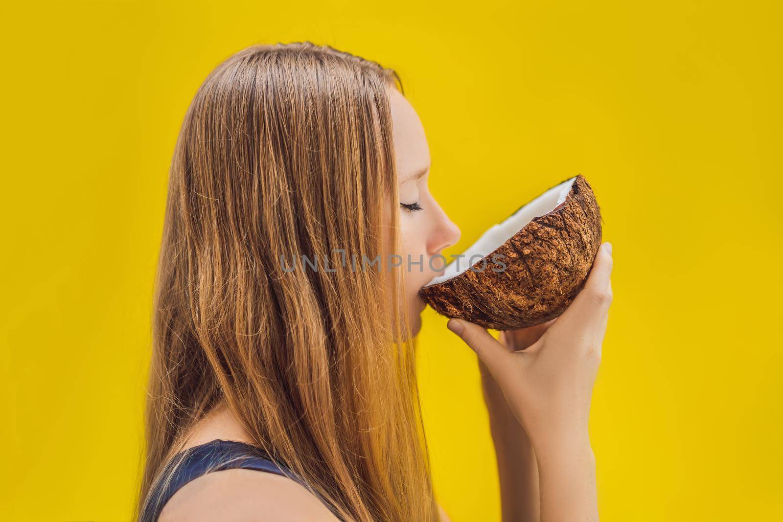 Young woman drinking coconut milk from coconut on a yellow background.